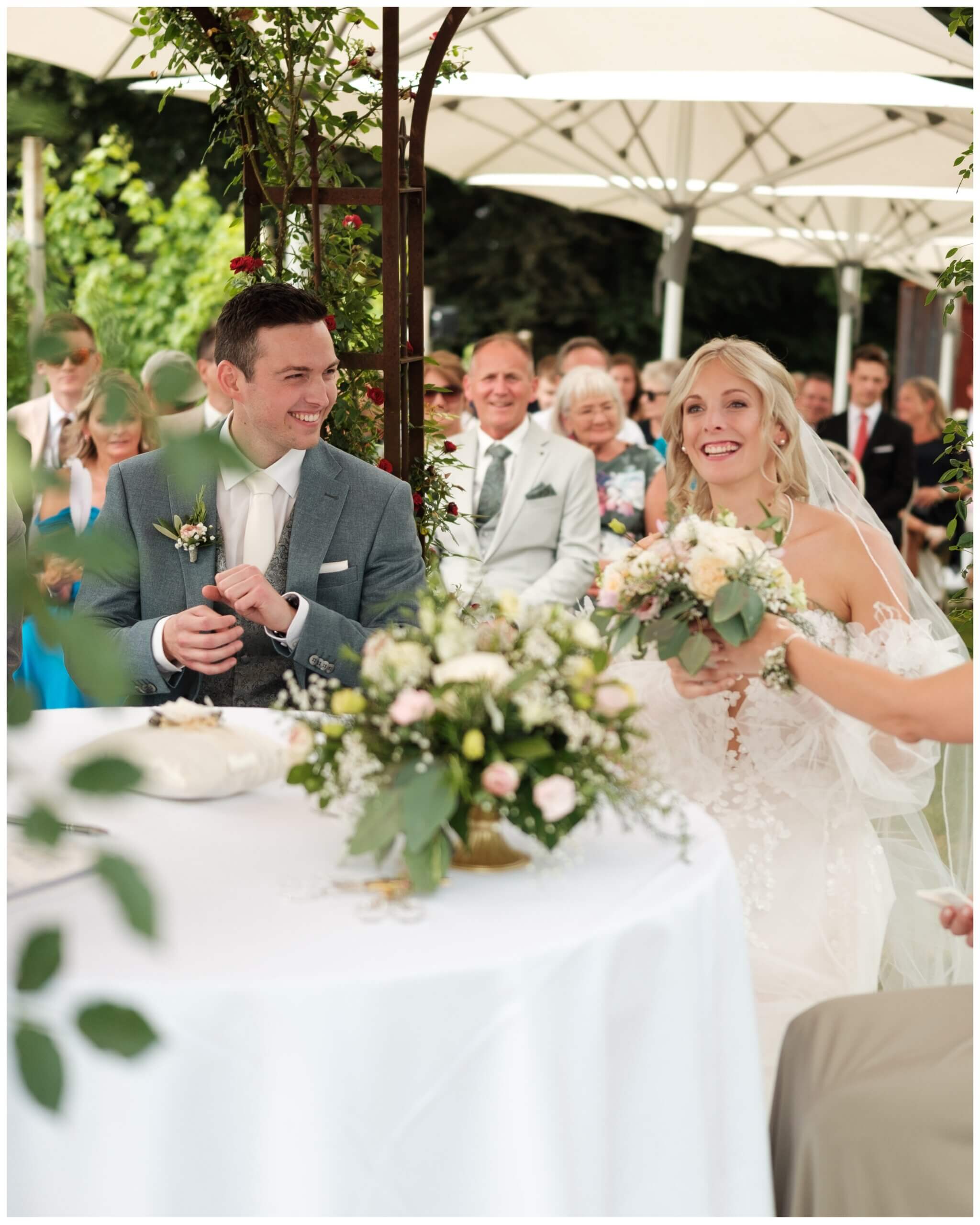 Braut lacht mit Gästen an der Hochzeitstafel